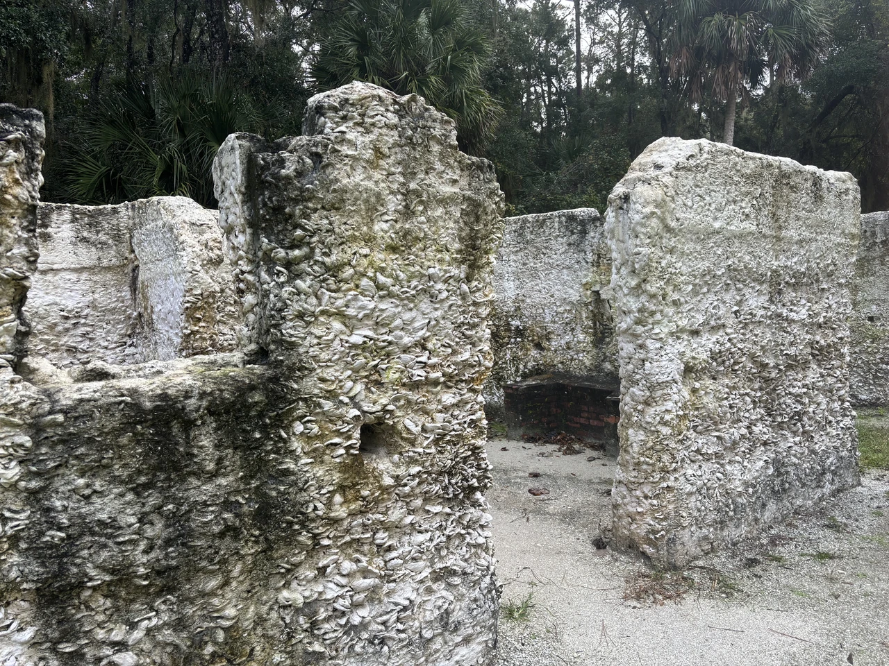 Shell-rich broken cabin walls frame an opening, with brick visible beyond it and bare ground below.