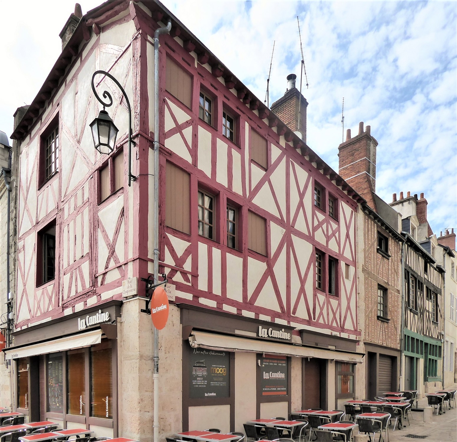 Red-painted crossed timber walls above shops on the corner of rue de la Poterne in Orléans, with pale panels and windows on both street fronts.
