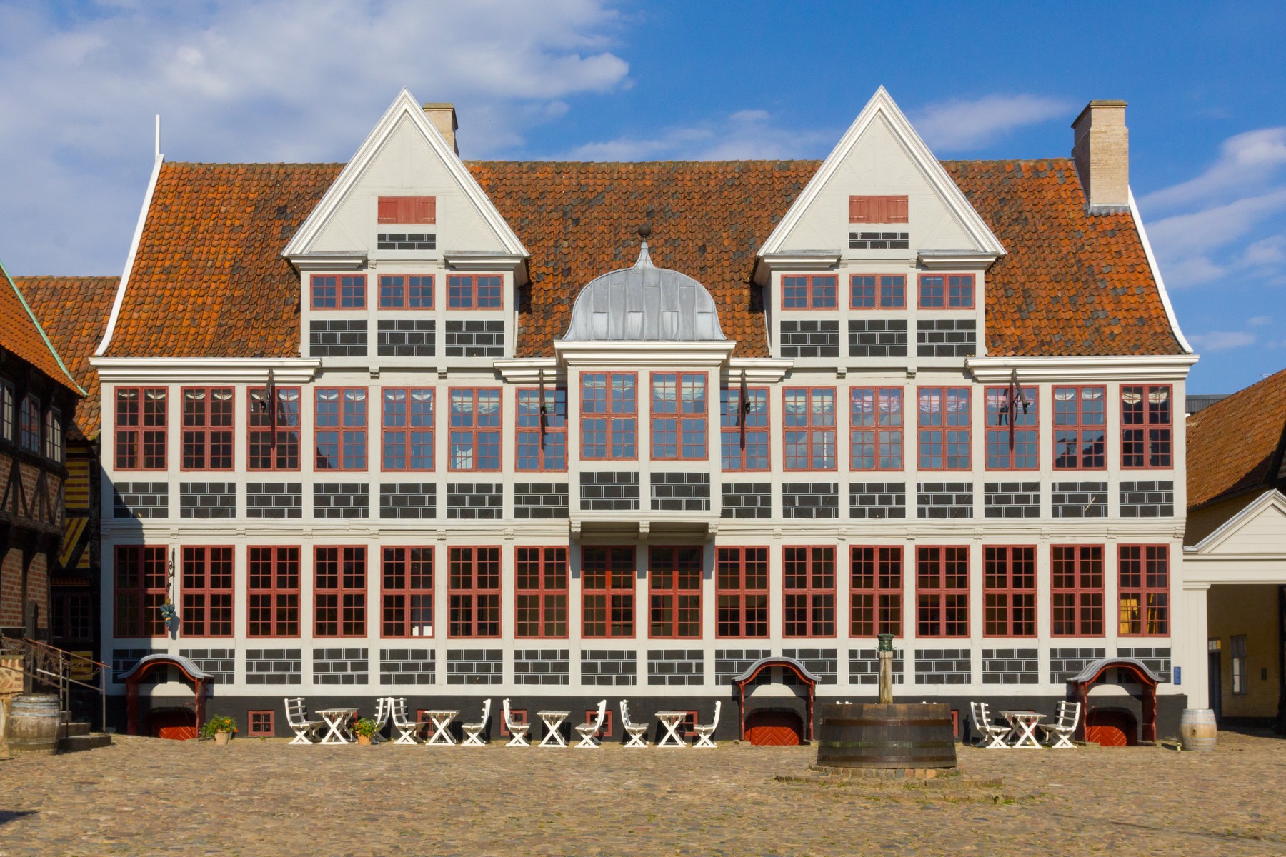 Møntmestergården at Den Gamle By, with two projecting gabled fronts, a central raised entrance, pale wall fields and red-brown window frames.