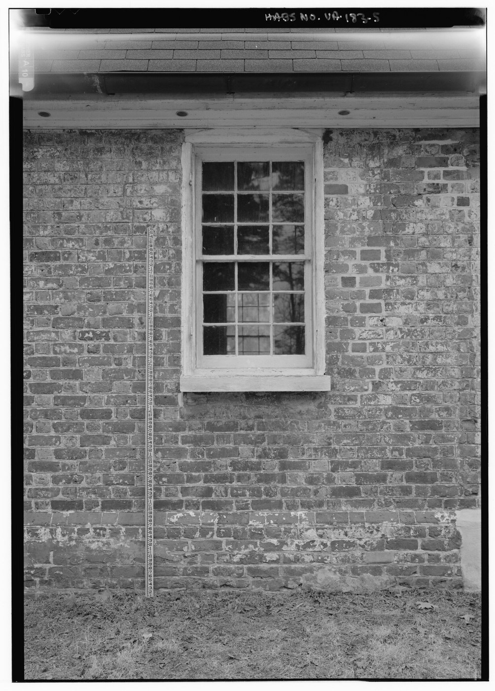 Black-and-white survey photograph of a historic brick wall, low window, repointing and measuring scale.