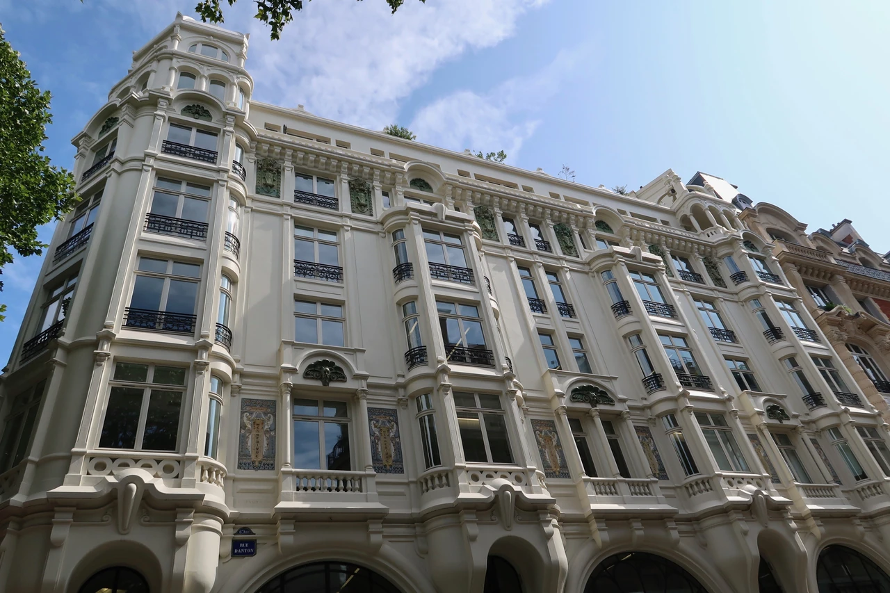 The pale street-corner facade at 1 rue Danton has projecting window bays, curved ornament and decorative ceramic panels.