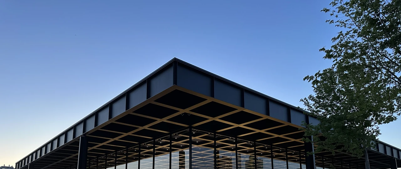 Neue Nationalgalerie’s broad gridded roof projects beyond its inset glazing, with a dark steel support beneath its edge.