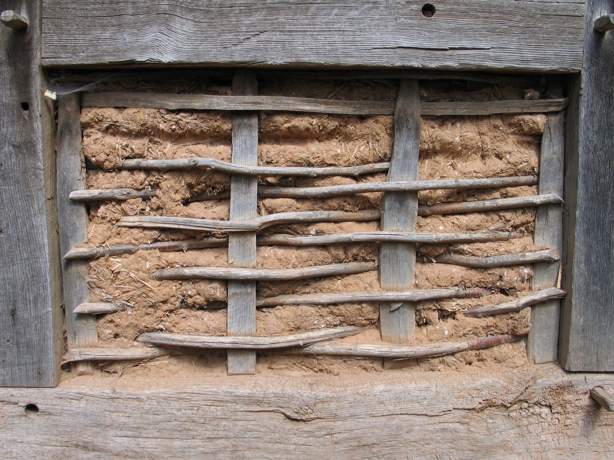 Fibrous earth within a timber frame, with exposed horizontal organic members crossing vertical staves.