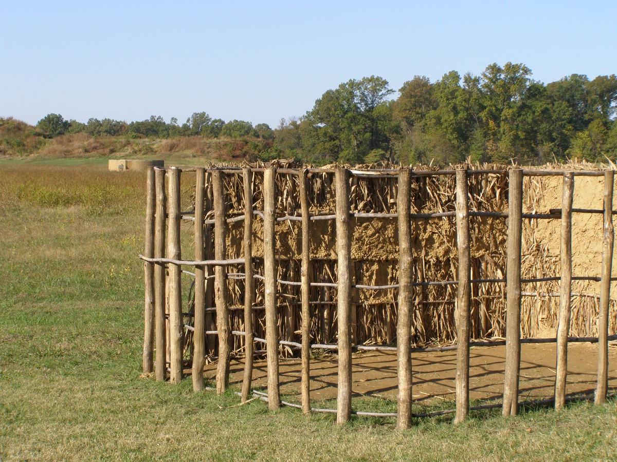 An Angel Mounds museum construction display with partly applied fibrous earth and bare vertical supports crossed by slender horizontal members.