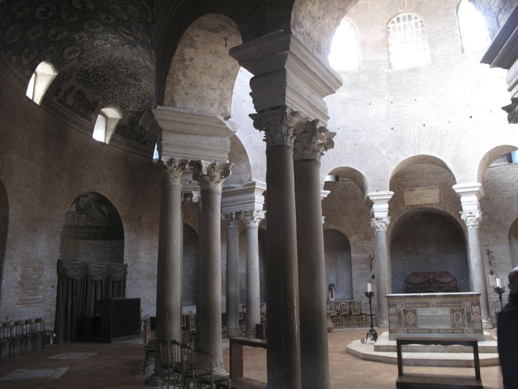 Paired columns divide a high central interior and altar from a lower curved passage beneath a dark mosaic vault.