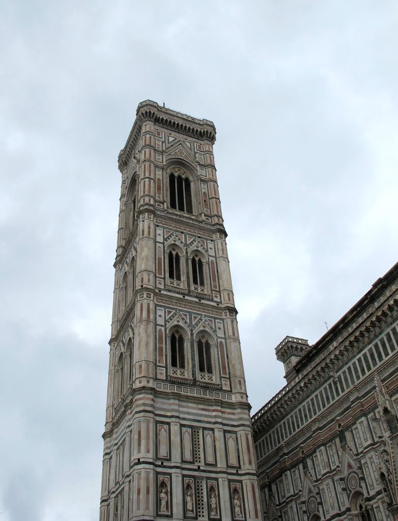 Patterned white, green and pink marble surrounds tall arched openings below a projecting terrace at the top of the tower.