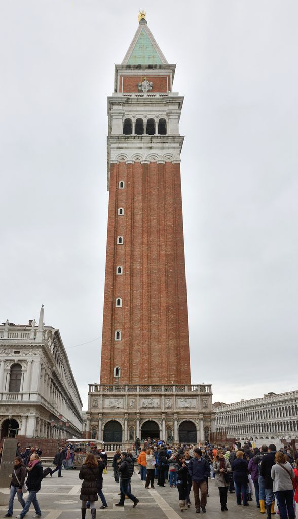 A tall red-brick shaft rises from the Loggetta to an open pale bell chamber, green spire and gilded angel above a crowded square.
