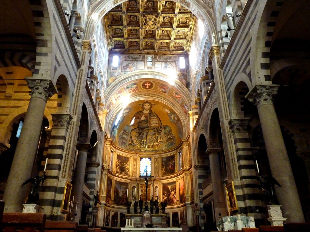 A curved gold mosaic apse closes an interior framed by striped arches and columns, beneath a coffered ceiling and above the altar area.