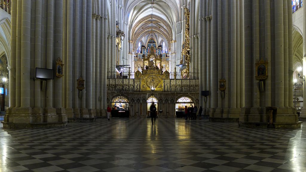 A sculpted enclosure spans the space between massive nave piers, beyond a broad chequered floor with passages visible at the sides.