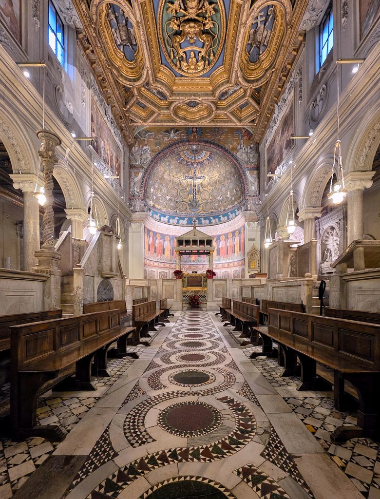 Marble screens and raised reading platforms surround a patterned central floor inside an arcaded nave, with wooden benches and the altar canopy farther ahead.