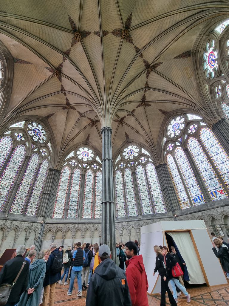 A slender central column supports ribs spreading across a high vault above traceried windows, visitors and a modern exhibition enclosure.