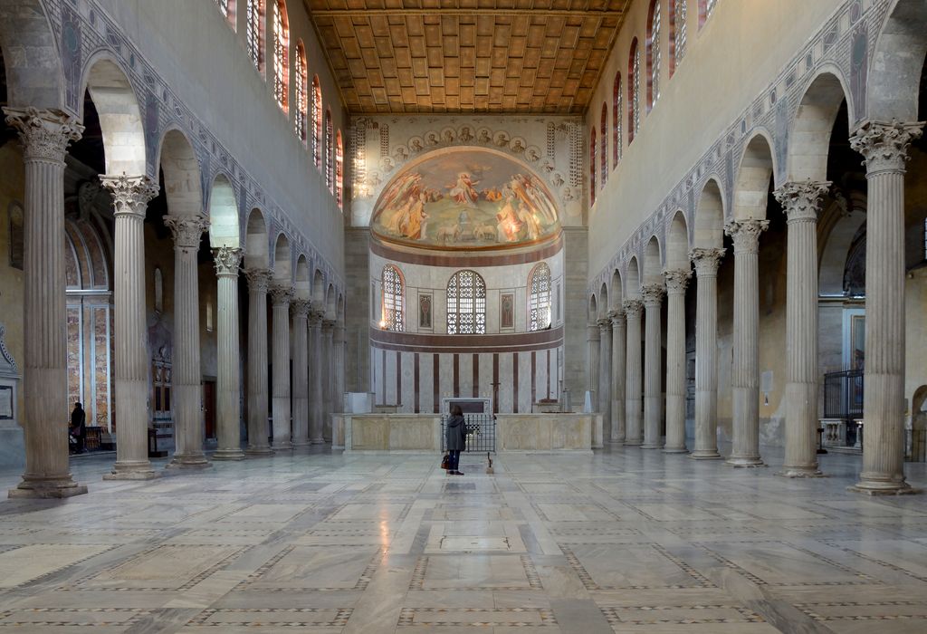 Two rows of columns and arches flank an open nave that ends at a screened sanctuary and curved apse beneath a timber ceiling.