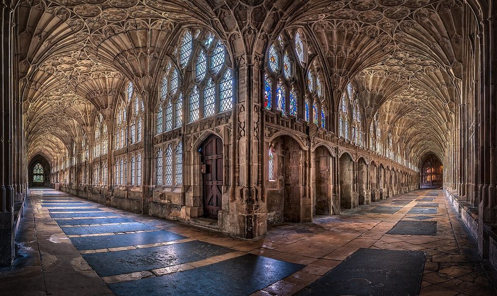 Two stone corridors meet at a corner, with radiating fan vaults above patterned paving and glazed openings.