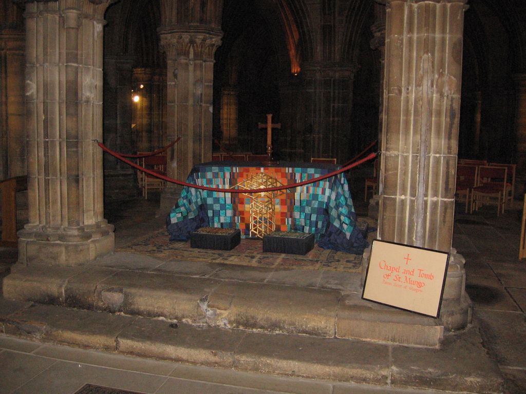A cloth-covered tomb setting stands between clustered stone piers, behind a rope barrier and above worn steps.