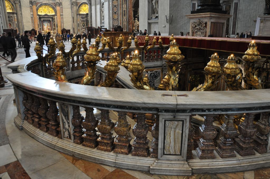 A curved marble balustrade and rows of lamps surround a recessed opening beside the altar and the base of the baldachin.