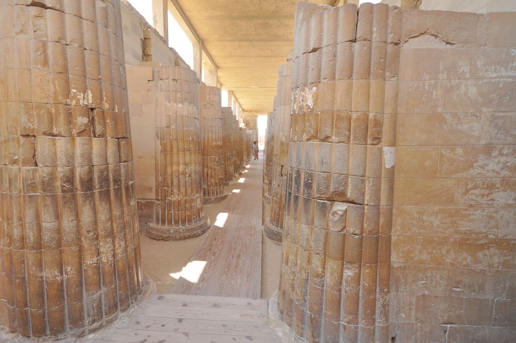 Rows of stone columns with bundled-stem profiles bordering a narrow roofed passage in Djoser’s complex at Saqqara.