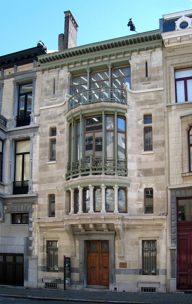 A narrow stone town-house façade with a projecting glazed centre, slender supports and iron railings.