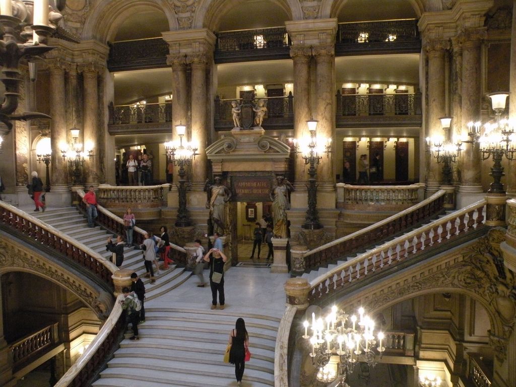 A broad marble stair divides into two curved flights beneath decorated galleries, columns and bright lamps.