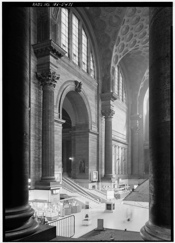 A historic black-and-white view frames a high coffered waiting room between giant columns, with stairs and kiosks below.