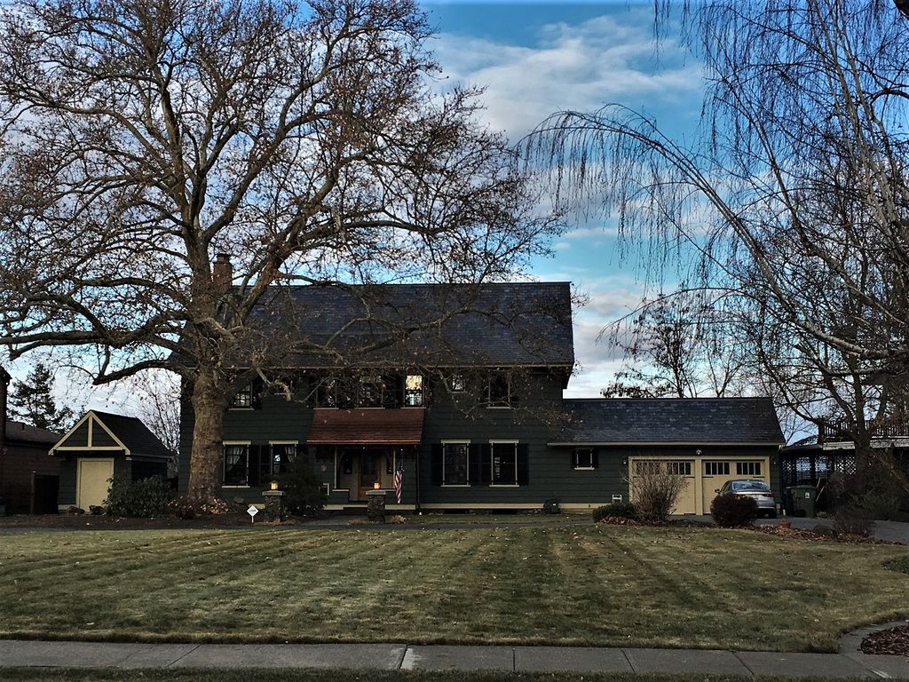 A dark shingled house with a broad sloping roof and flared eaves has a central porch and rows of windows, with a lower garage wing at right.
