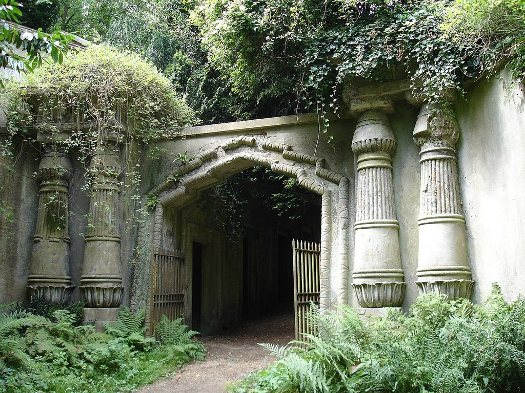 Paired carved columns and a decorated lintel frame a dark passage beneath thick vegetation.