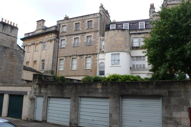 Different stone rear façades, projecting bays, sash windows and roof heights above a row of garage doors.