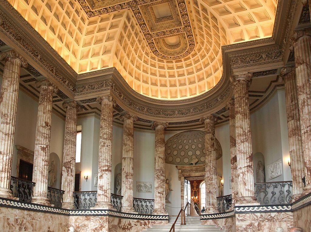 A broad stair rises between classical columns beneath a richly coffered ceiling.