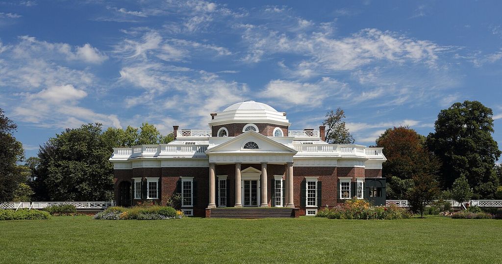 A brick house with a low dome and columned portico stands above a lawn.