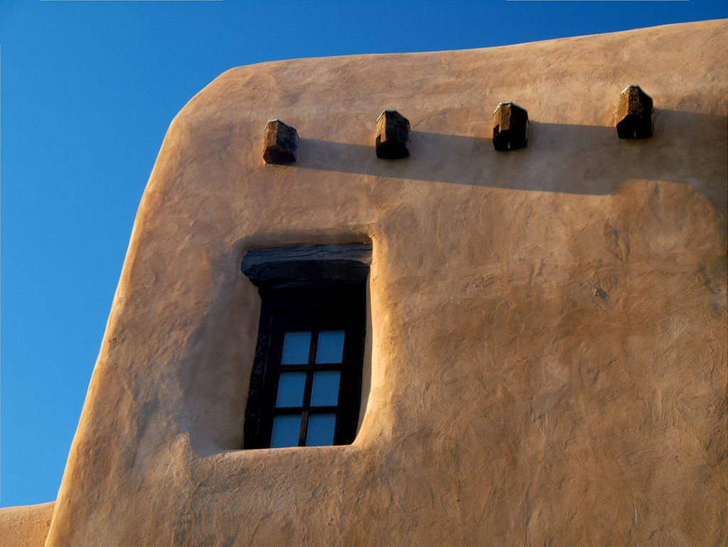 Four timber ends project above a dark recessed window in a textured, rounded wall.