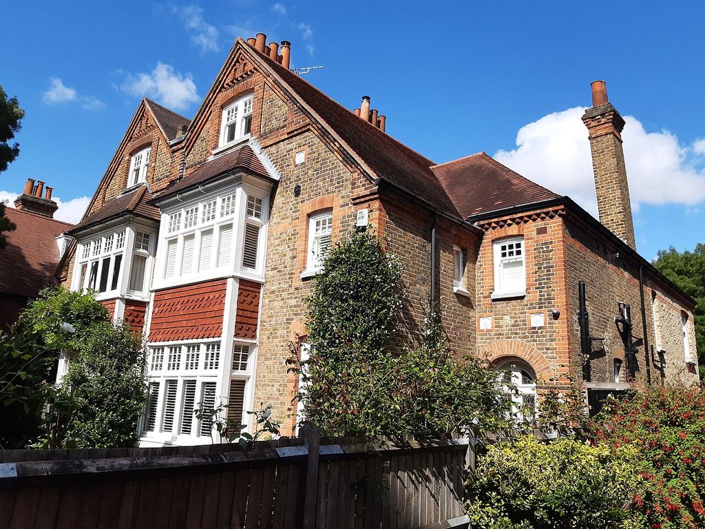 Paired brick gables rise above white projecting windows, red tile hanging and garden shrubs.
