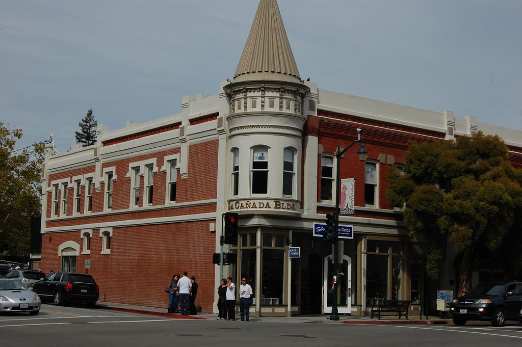 A circular bay with a conical roof projects above a glazed shop entrance where two brick street façades meet.