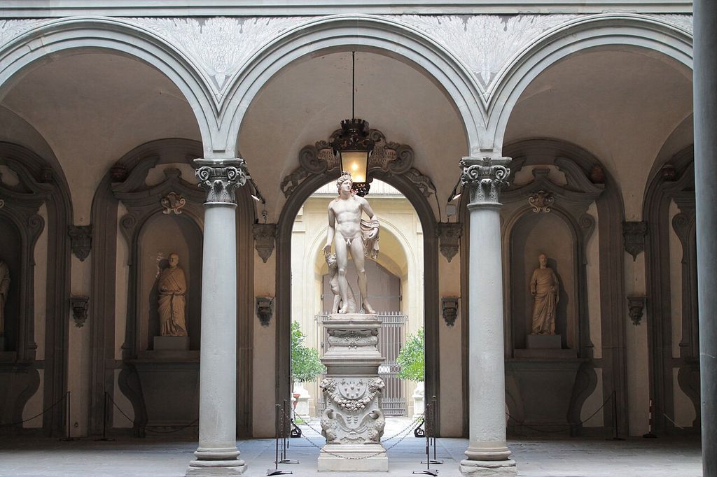 Round courtyard arches supported by columns, framing sculpture and a passage through Palazzo Medici-Riccardi.