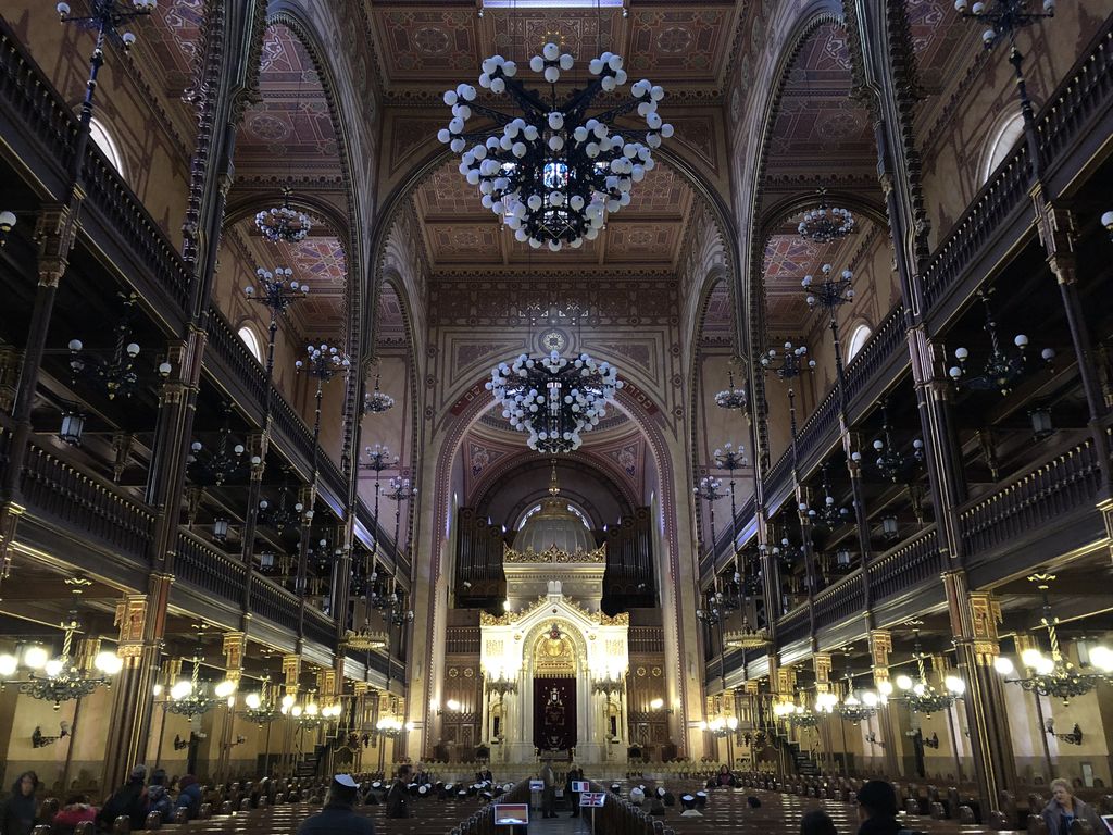 Two tiers of galleries flank a tall decorated interior with arches, chandeliers and rows of seating.