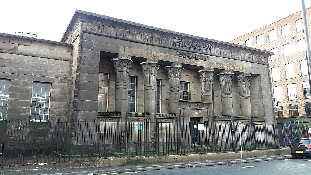 Large stone columns with plant-shaped capitals frame recessed windows beneath winged-disc carvings and a coved cornice.