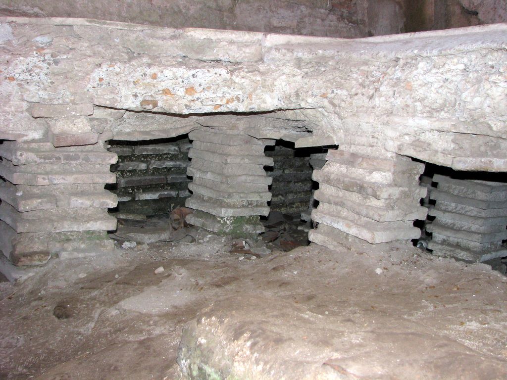Short stacks of bricks supporting the edge of a raised floor above an open heating cavity at Ostia Antica.