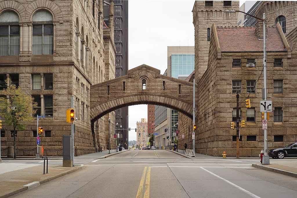 A masonry passage on a broad arch spans a street between two heavy stone buildings.