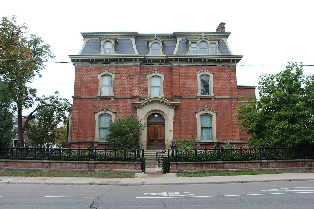 A symmetrical red-brick house has a central stone entrance, arched window hoods and three dormers in a mansard roof.
