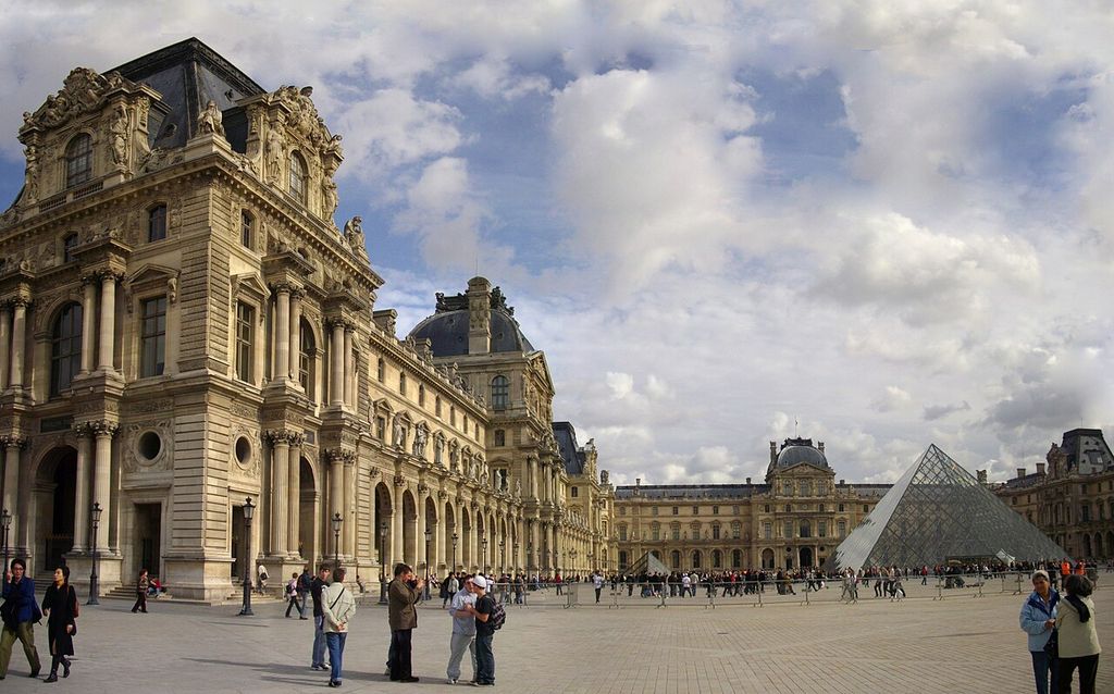 Sculpted stone pavilions with steep slate roof faces border a large courtyard containing a modern glass pyramid.