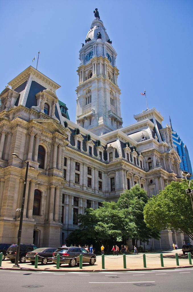 A tall clock tower and statue rise above ornate mansard pavilions and marble-faced wings.