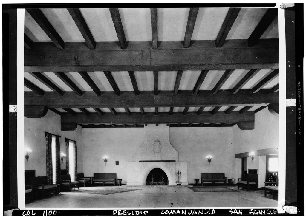 A black-and-white hall has heavy ceiling beams, benches along the walls and a broad fireplace at the far end.