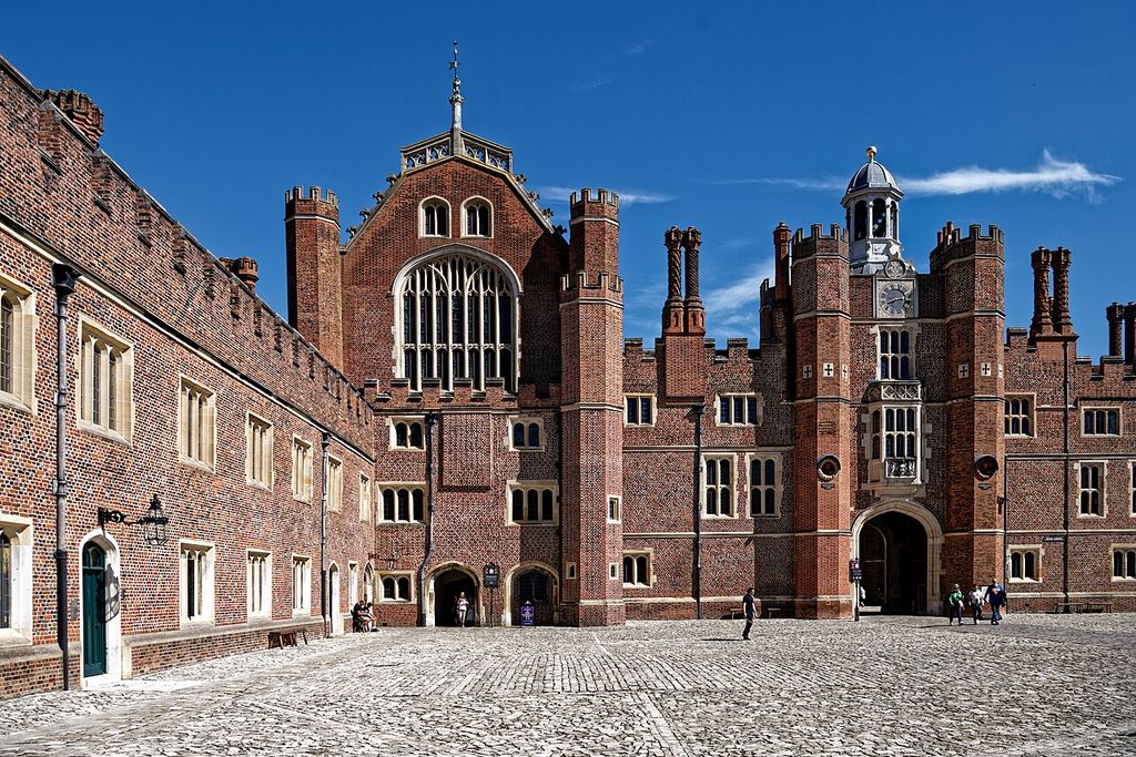Brick ranges, a large traceried window and a turreted gateway enclose a paved courtyard.