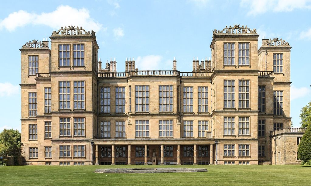 Large grids of windows cover a symmetrical stone house with projecting towers and ES lettering on its parapets.