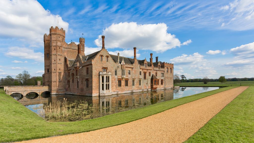 A tall crenellated brick tower rises beside stepped gables and chimneys above a moat, with a bridge at the left.