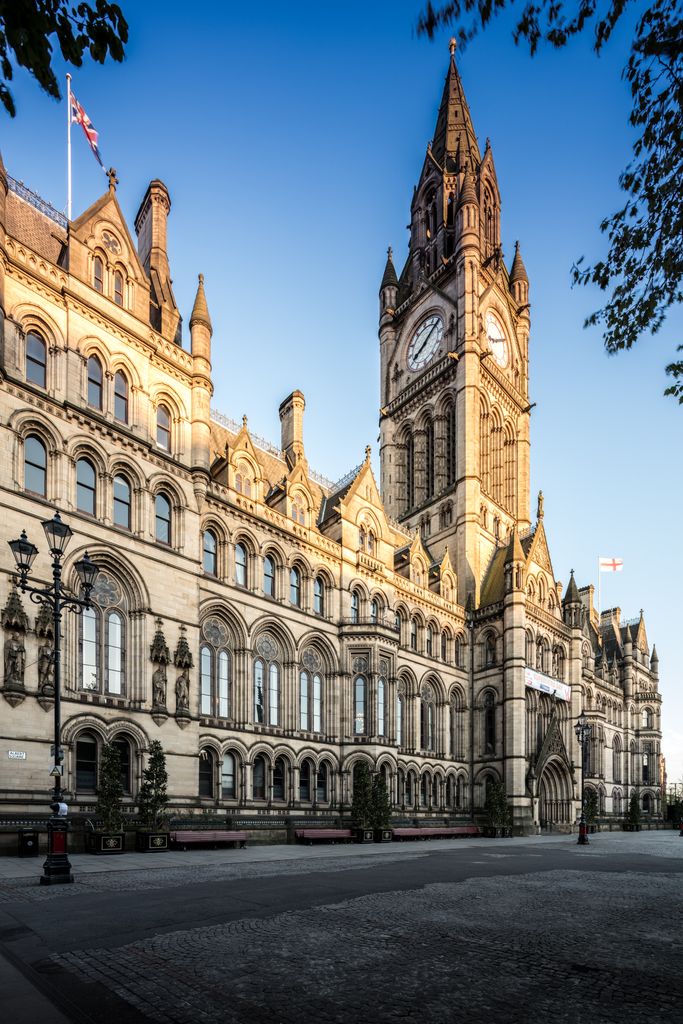 A tall clock tower rises over a long stone frontage with Gothic entrances, arcaded windows, tracery and steep gables.