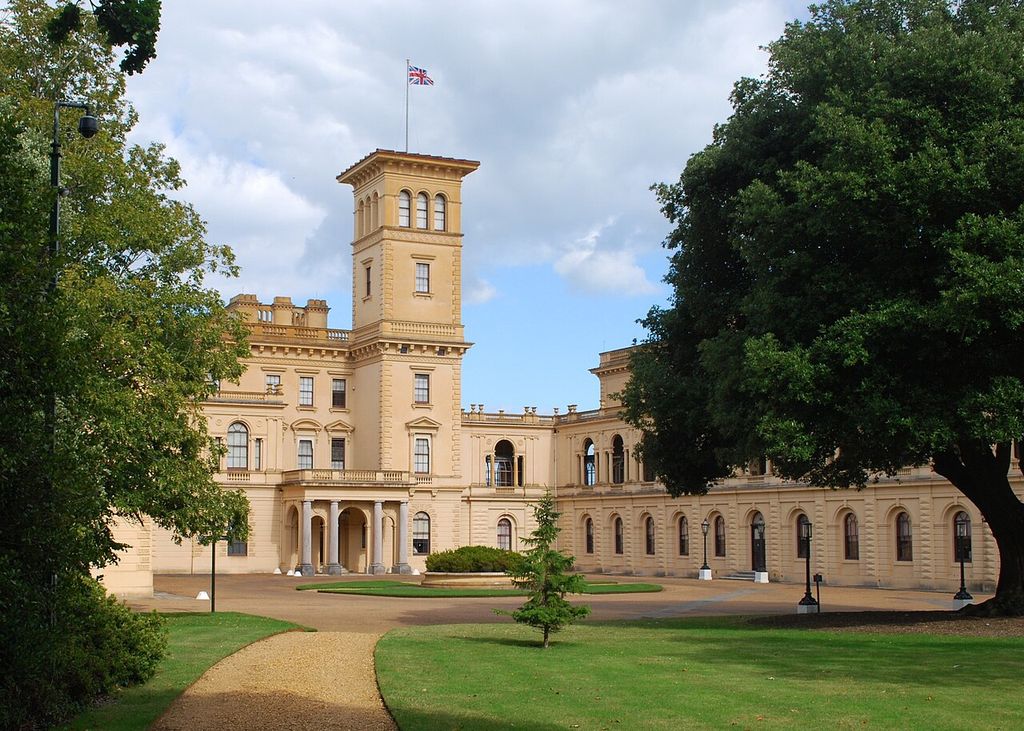 A square Italianate tower with deep eaves rises above pale walls, arched windows and a columned entrance.