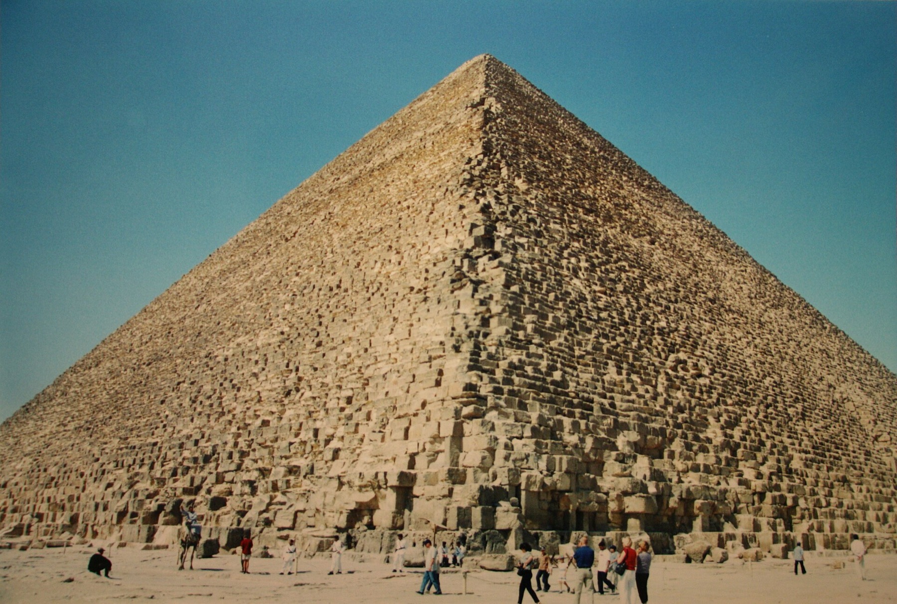 Close low-angle view of the Great Pyramid of Khufu showing two stone faces meeting at the apex under a blue sky.