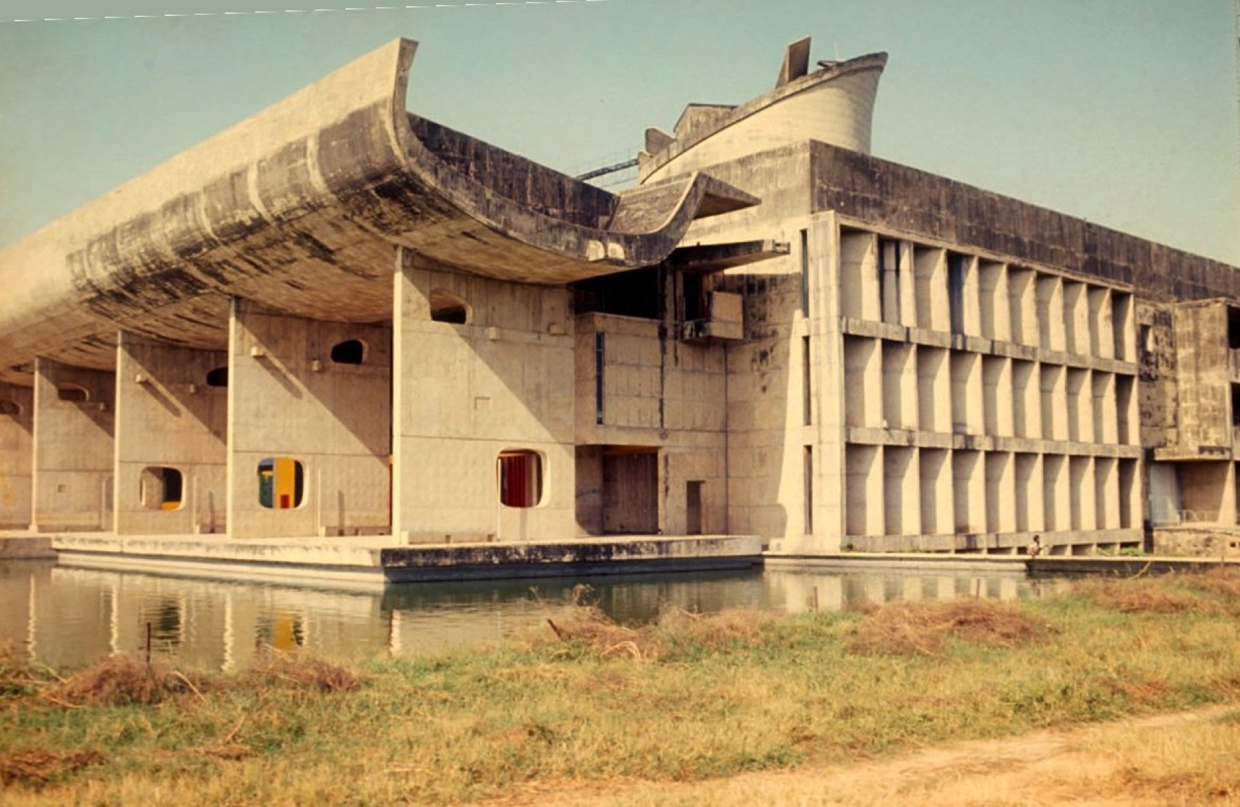 Palace of Assembly at Chandigarh with curved concrete portico, brise-soleil, reflecting pool and roof forms.