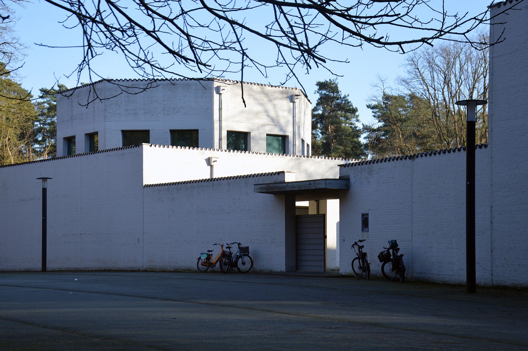 Roosenberg Abbey entrance court with white brick walls, square openings, shallow roofs and bicycles.