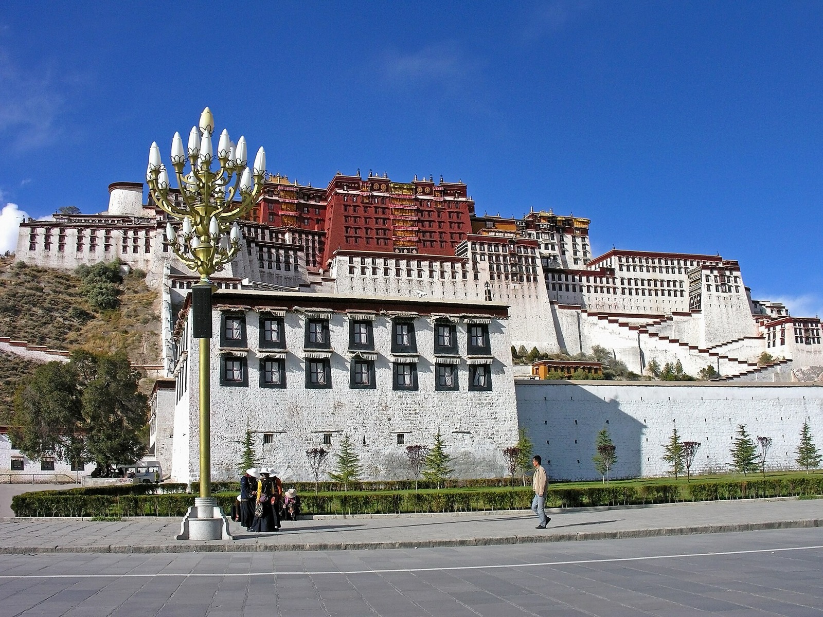 Potala Palace above Lhasa street, red centre and white wings rising from Red Mountain behind a foreground lamp and buildings.