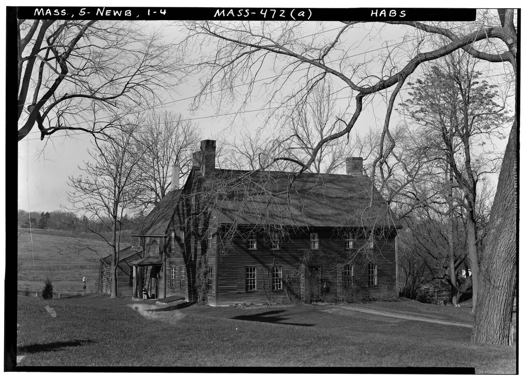 An oblique monochrome view shows a timber house with adjoining roof volumes, chimneys, windows and an entrance beneath bare tree branches.